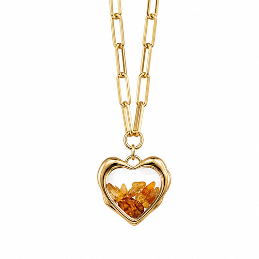 A gold heart-shaped pendant necklace featuring preserved amber-colored flower petals inside a clear, heart-shaped frame, suspended from a gold paperclip chain on a white background.