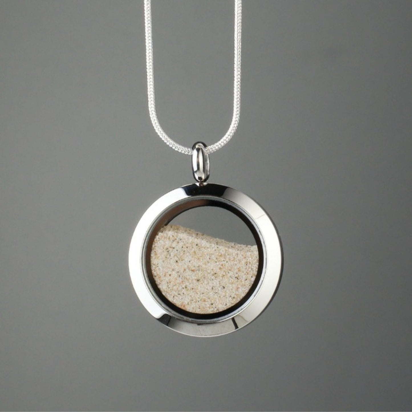 andmade beach sand amulet with genuine beach sand encased under glass and set in stainless steel, symbolizing the flow of time and the importance of cherishing the present.