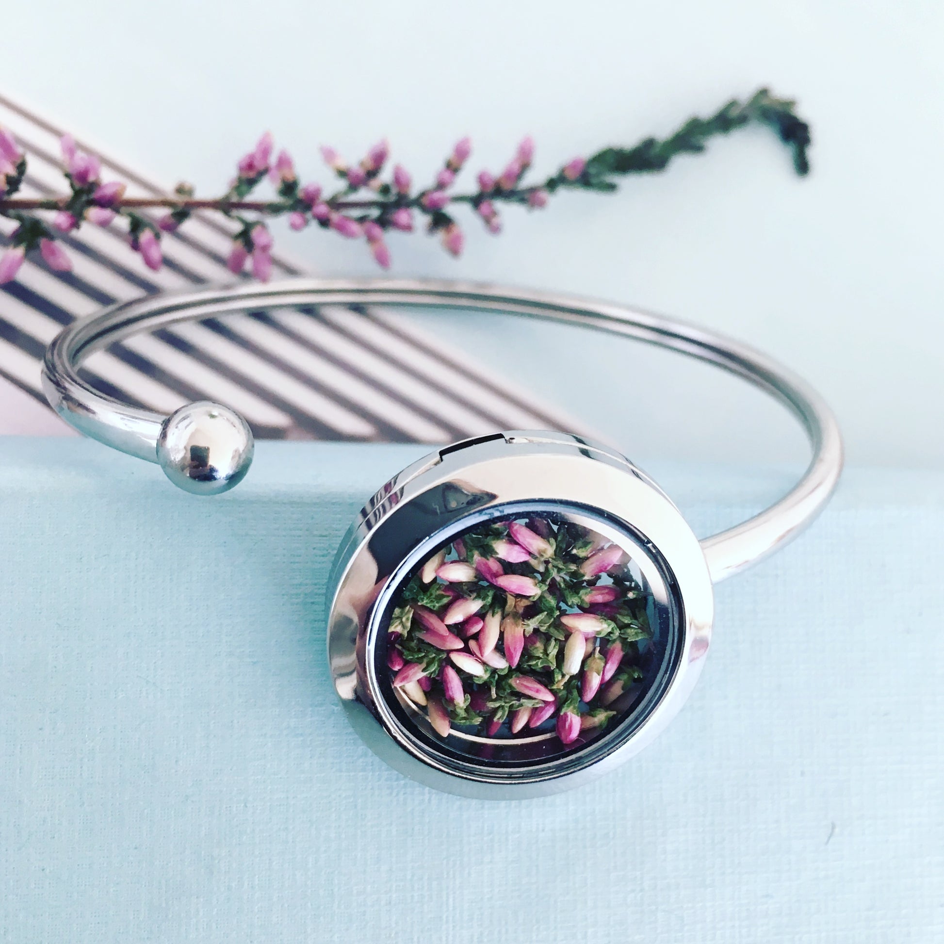 Handmade cuff bracelet with real heather flowers encased under glass, symbolizing endurance and healing.